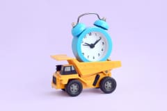 A dump truck loaded with an alarm clock on pastel lilac background. The concept of optimization and rational time management. Saving of time and delegation of work