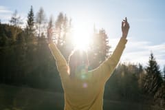 woman enjoying financial independence. her arms raised high and bright sun shining just above her head.