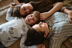 High angle view of little boy smiling at camera while lying on bed with his homosexual mothers