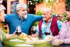 Genuine retired people having fun drinking red wine at dinner party - Senior friends eating together outside at restaurant - Dinning life style concept on vivid filter - Focus on bearded hipster man