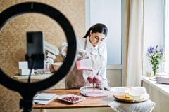 Side Hustle Ideas to Make Money, Culinary online courses. Central Asian Arabic woman pastry chef making cake and record video on smartphone in home kitchen