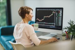 Middle age woman trading with cryptocurrency while working on computer at home office.She is monitors her investments in the stock markets.